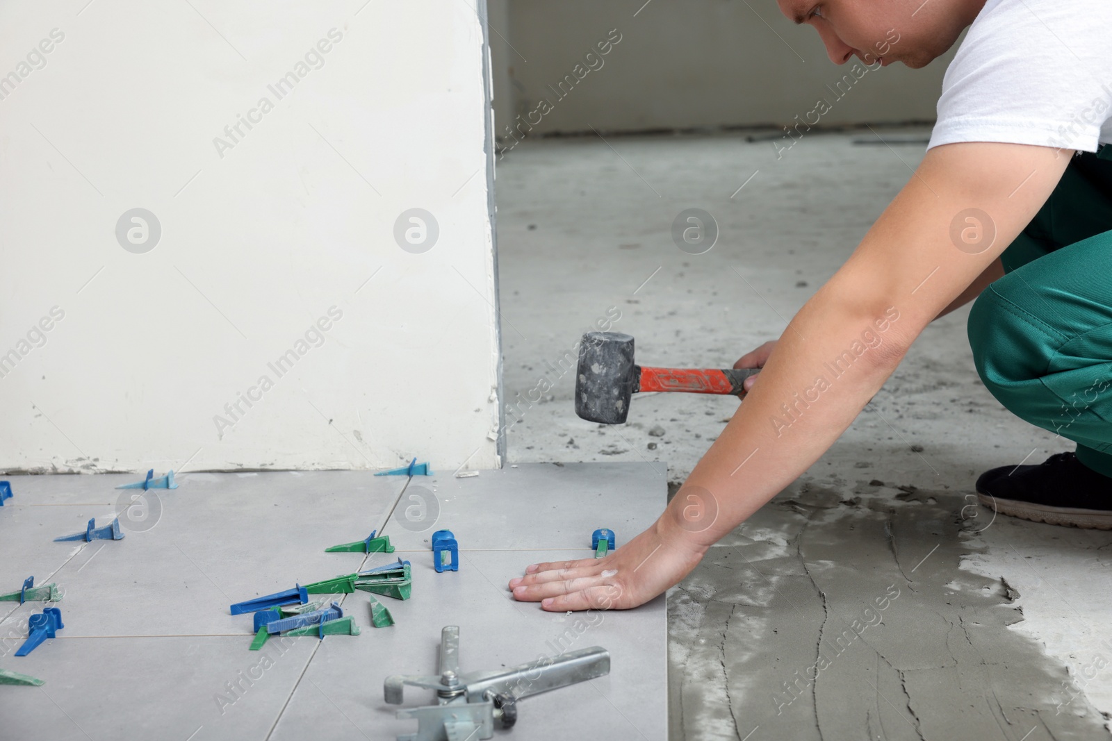 Photo of Worker with rubber hummer installing tiles indoors , closeup