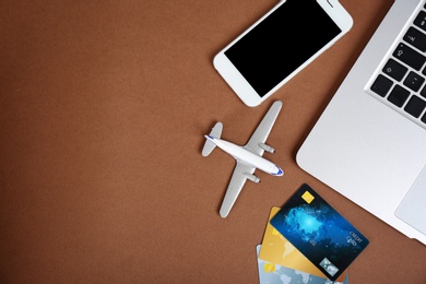 Smartphone, laptop, credit cards and toy plane on color background, flat lay with space for text. Travel agency