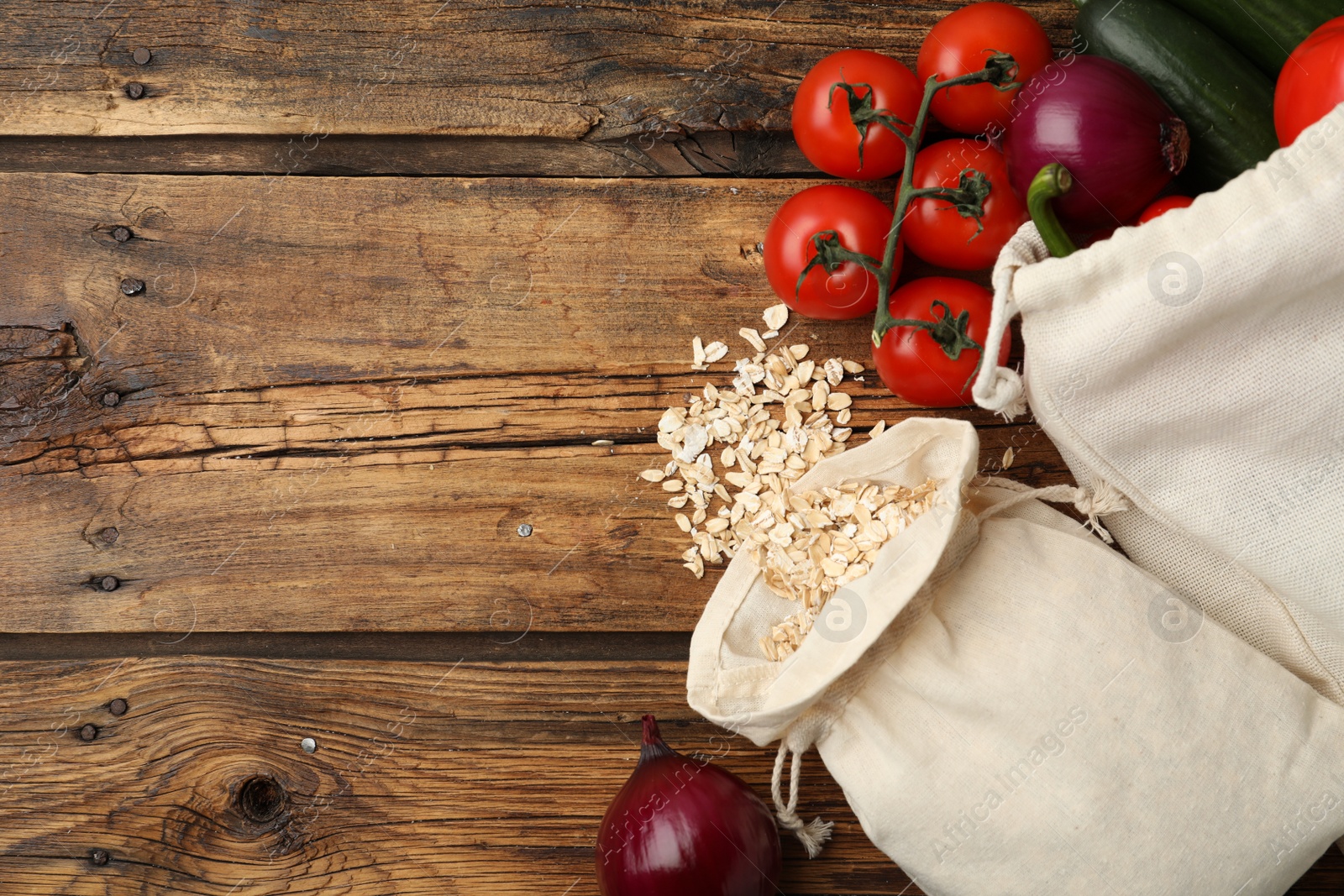 Photo of Cotton eco bags with vegetables and oat flakes on wooden table, flat lay. Space for text