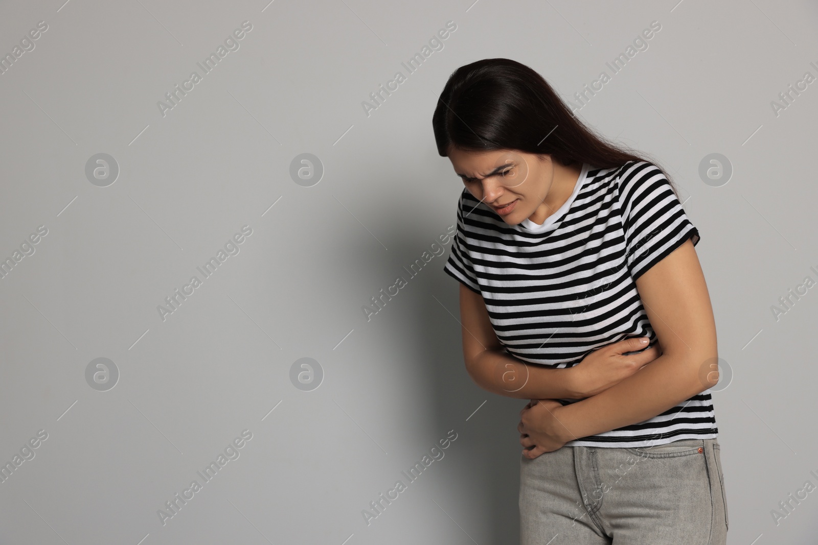 Photo of Young woman suffering from menstrual pain on grey background, space for text