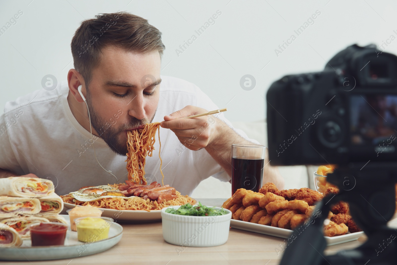 Photo of Food blogger recording eating show on camera against light background. Mukbang vlog