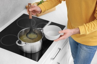 Man pouring delicious soup into bowl in kitchen, closeup