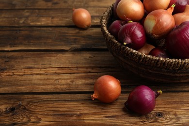Photo of Onion bulbs and basket on wooden table. Space for text
