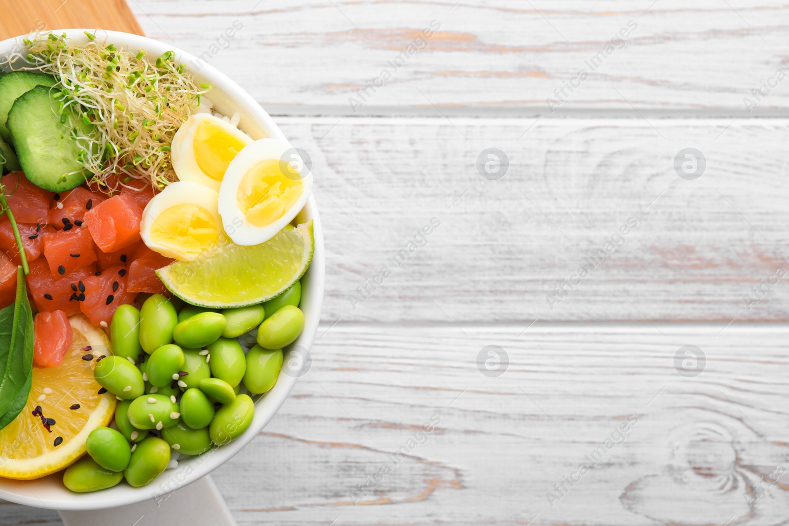 Photo of Delicious poke bowl with quail eggs, fish and edamame beans on white wooden table, top view. Space for text