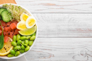 Delicious poke bowl with quail eggs, fish and edamame beans on white wooden table, top view. Space for text