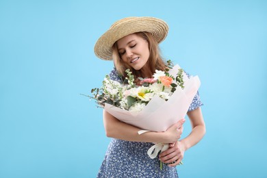 Photo of Beautiful woman in straw hat with bouquet of flowers on light blue background