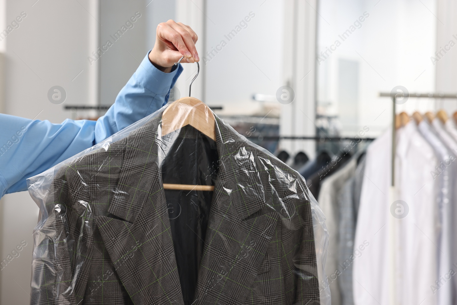 Photo of Dry-cleaning service. Woman holding jacket in plastic bag indoors, closeup and space for text