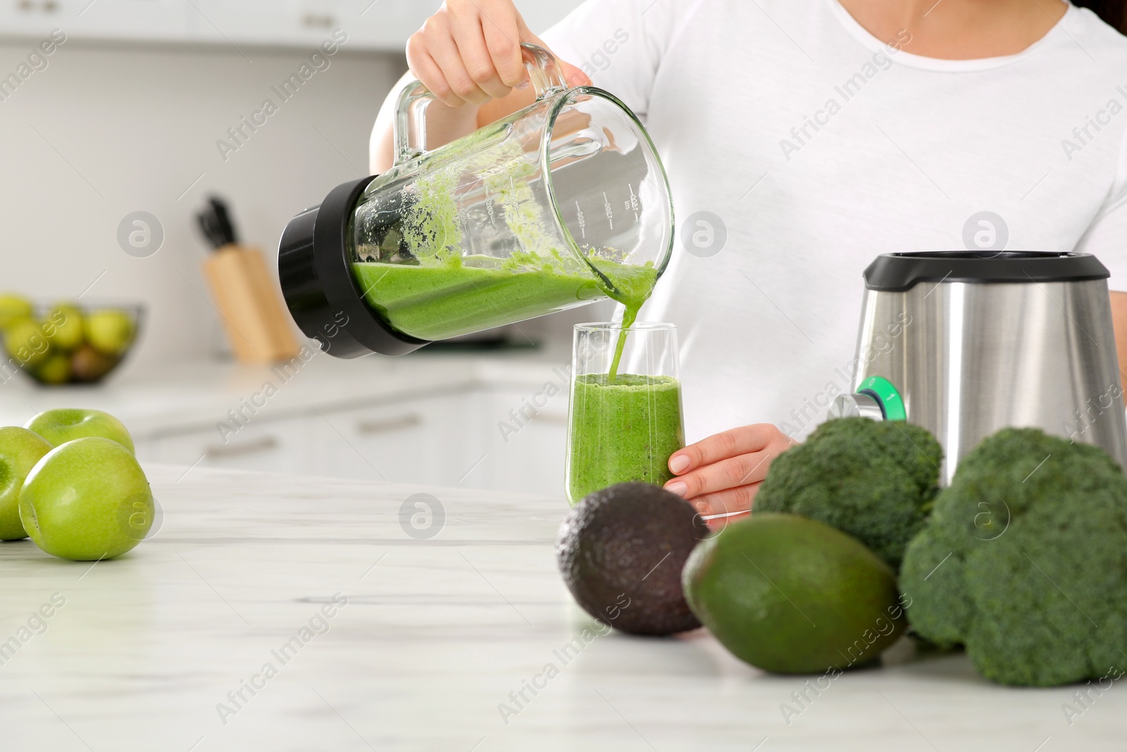 Photo of Woman pouring tasty smoothie into glass at white table in kitchen