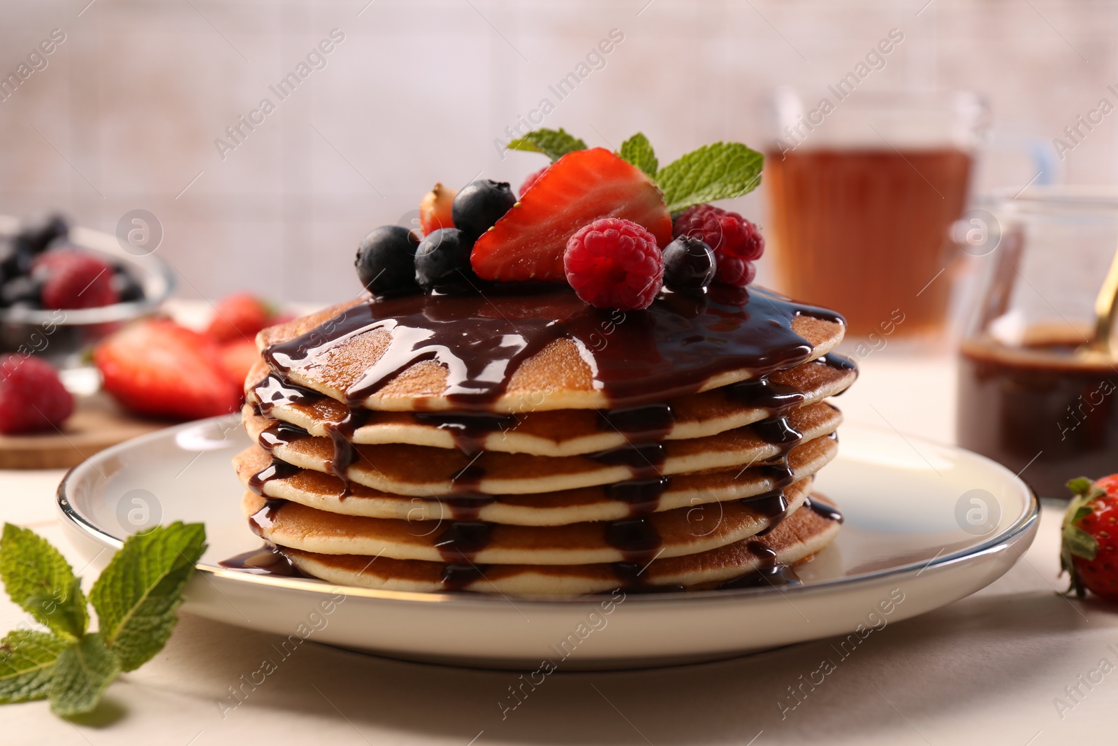 Photo of Stack of tasty pancakes with fresh berries, chocolate sauce and mint on white table, closeup
