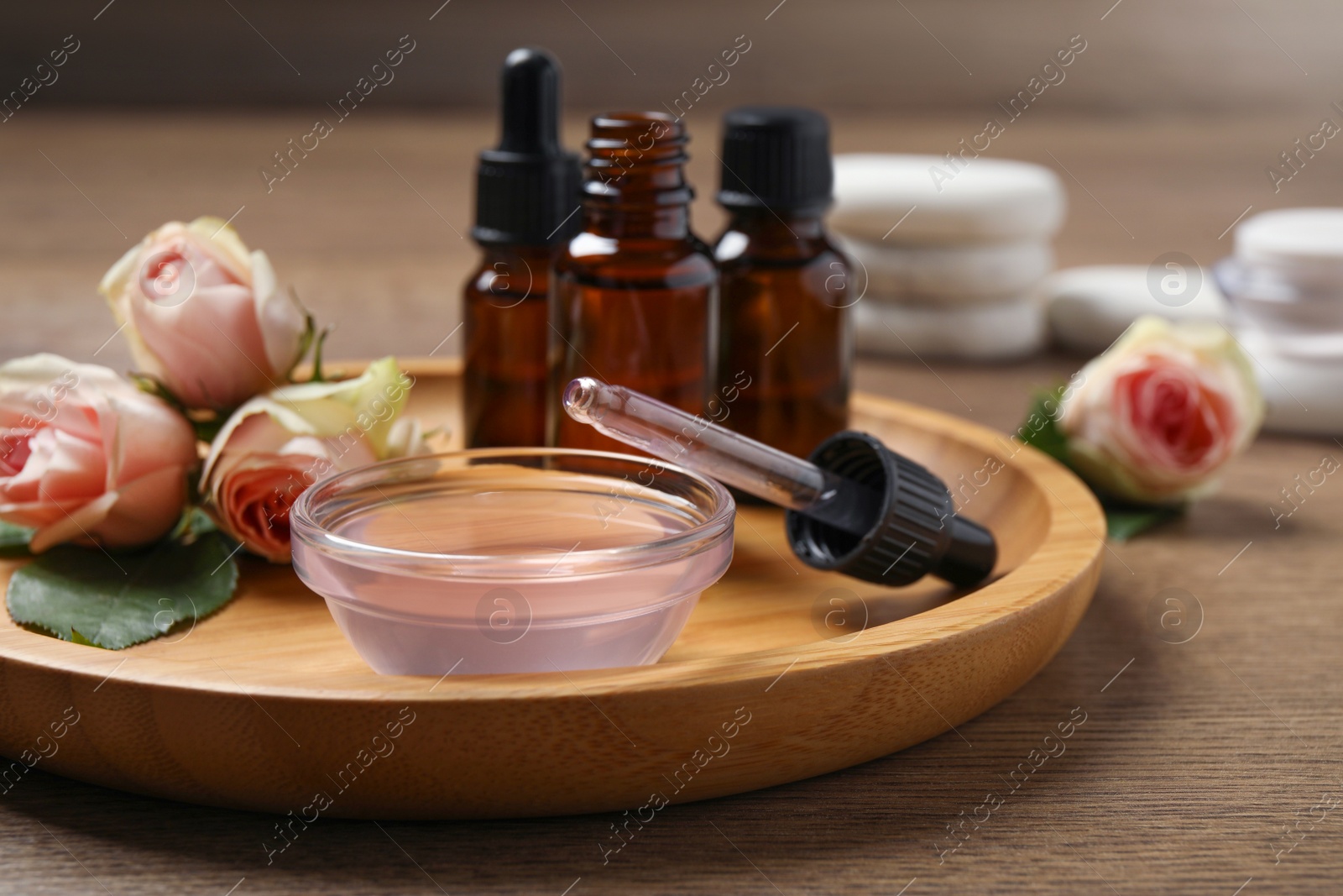 Photo of Rose essential oil and flowers on wooden table