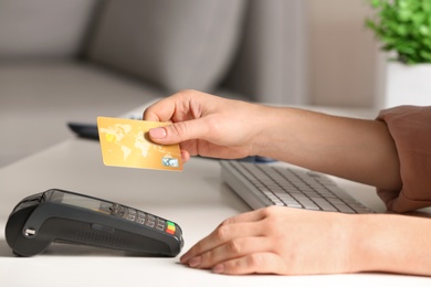 Photo of Woman using modern payment terminal at table indoors, closeup