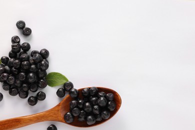 Spoon with ripe bilberries and leaf on white background, flat lay. Space for text