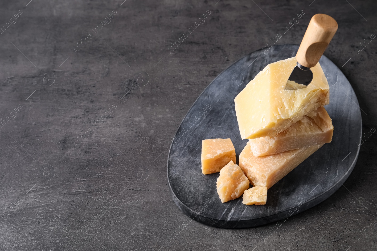 Photo of Parmesan cheese with board and knife on grey table. Space for text