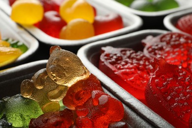 Photo of Different delicious gummy candies in containers, closeup