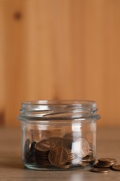 Glass jar with coins on wooden table, closeup