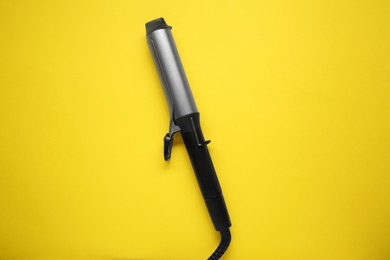 Photo of Hair curling iron on yellow background, top view