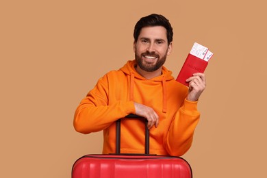 Smiling man with passport, suitcase and tickets on beige background