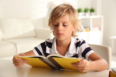 Photo of Little boy doing homework at table indoors