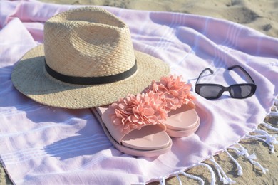 Photo of Blanket with stylish slippers, sunglasses and straw hat on sandy beach