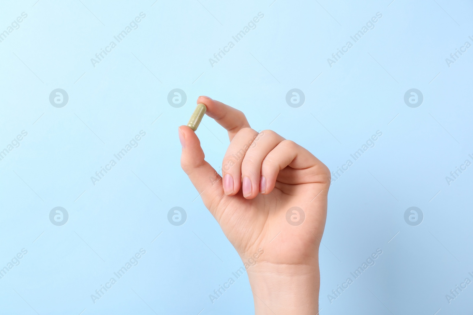 Photo of Woman holding vitamin capsule on light blue background, closeup
