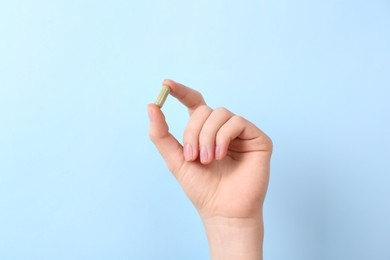 Woman holding vitamin capsule on light blue background, closeup