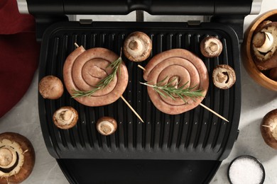 Photo of Electric grill with homemade sausages, rosemary and mushrooms on marble table, flat lay