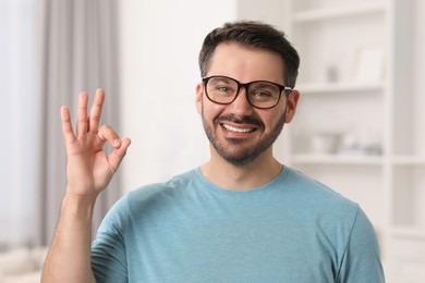 Photo of Portrait of happy man in stylish glasses showing OK gesture at home