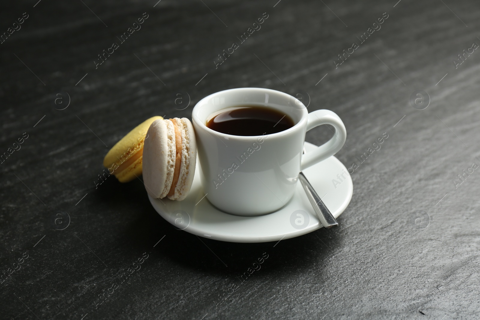 Photo of Hot coffee in cup, macarons and saucer on dark textured table