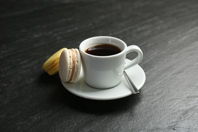Hot coffee in cup, macarons and saucer on dark textured table