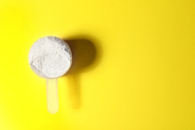 Scoop of protein powder on yellow background, top view with space for text