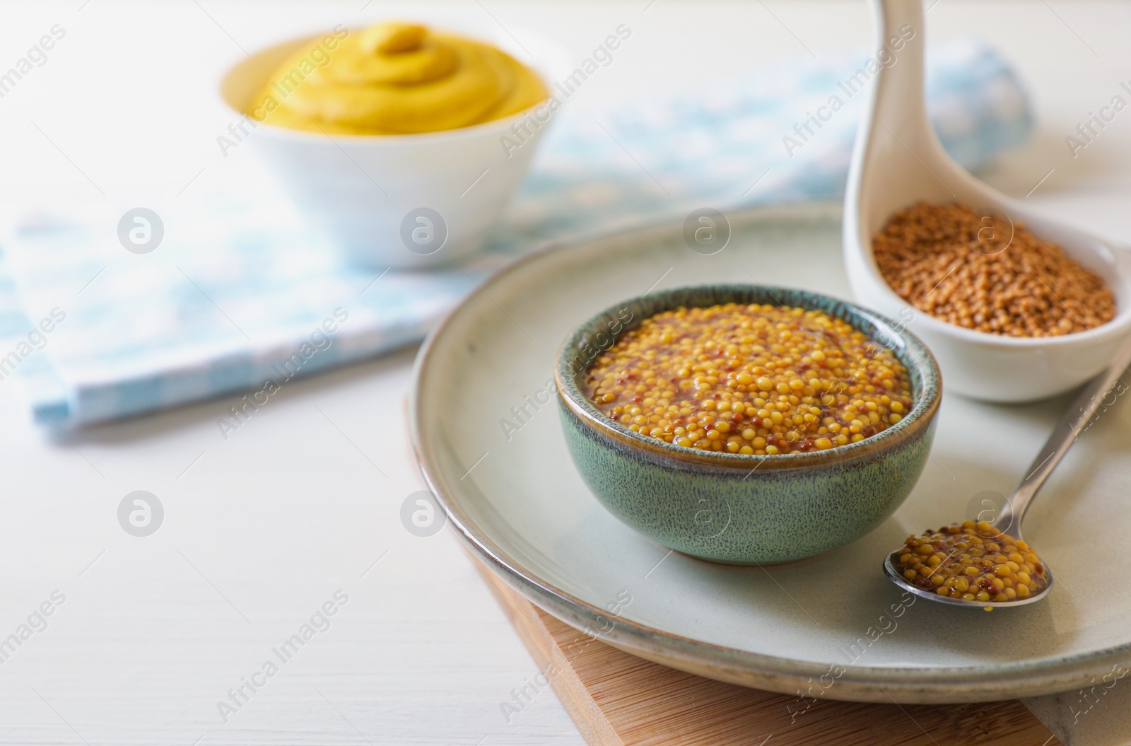 Photo of Bowl and spoon of whole grain mustard on white wooden table. Space for text