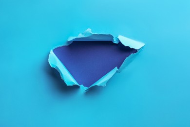 Photo of Hole in light blue paper on color background