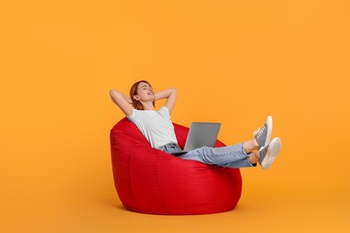Photo of Smiling young woman with laptop sitting on beanbag chair against yellow background