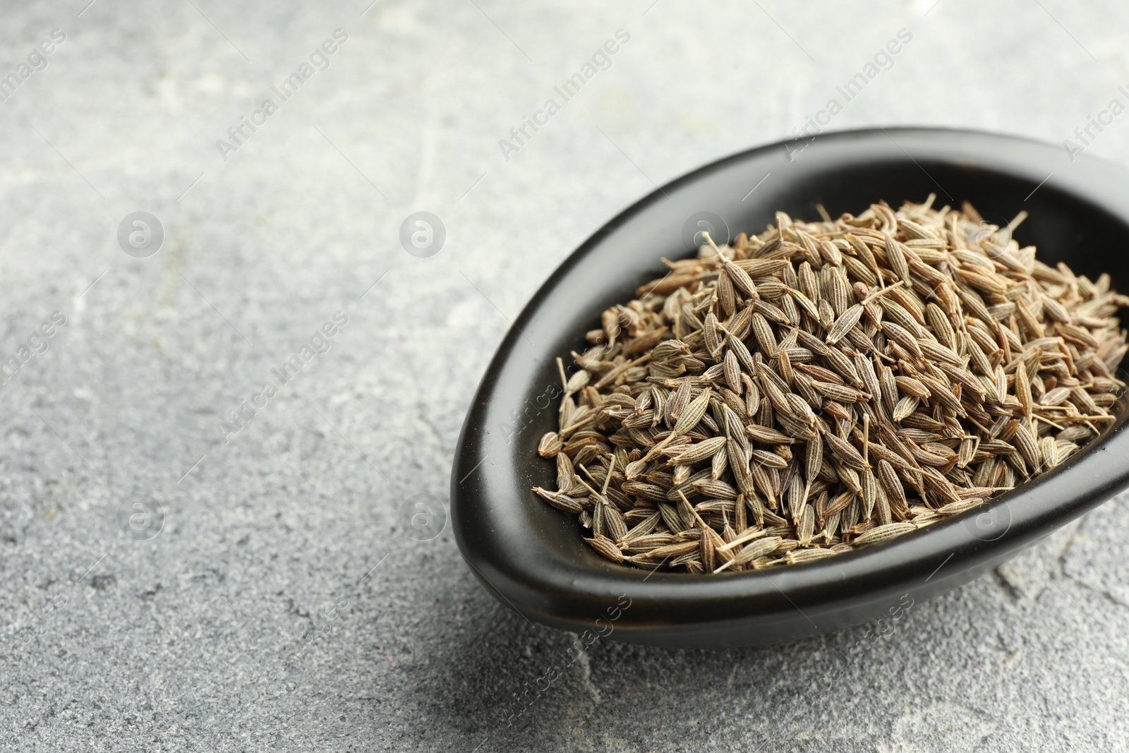 Photo of Caraway seeds in bowl on grey table, closeup. Space for text
