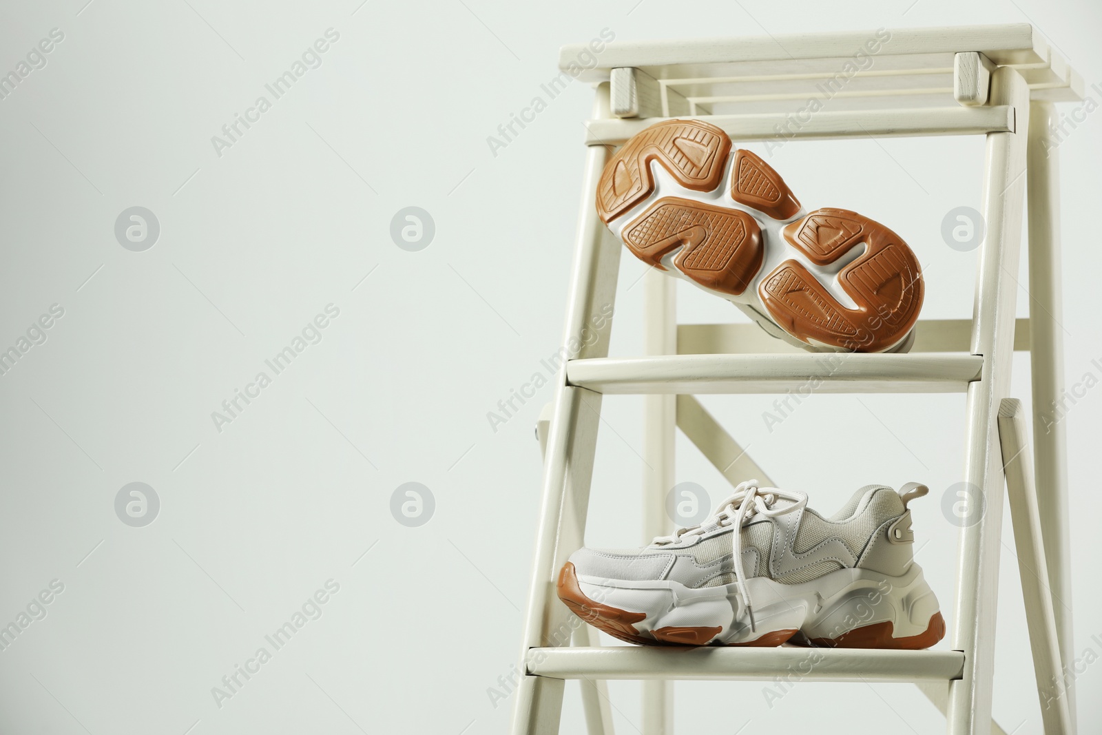 Photo of Stylish presentation of trendy sneakers on ladder against white background. Space for text