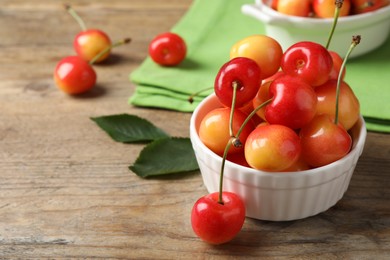 Photo of Sweet red cherries in bowl on wooden table, space for text