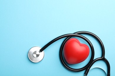 Stethoscope and red heart on light blue background, top view. Space for text