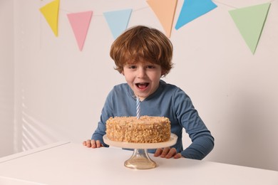 Cute boy with birthday cake at white table indoors