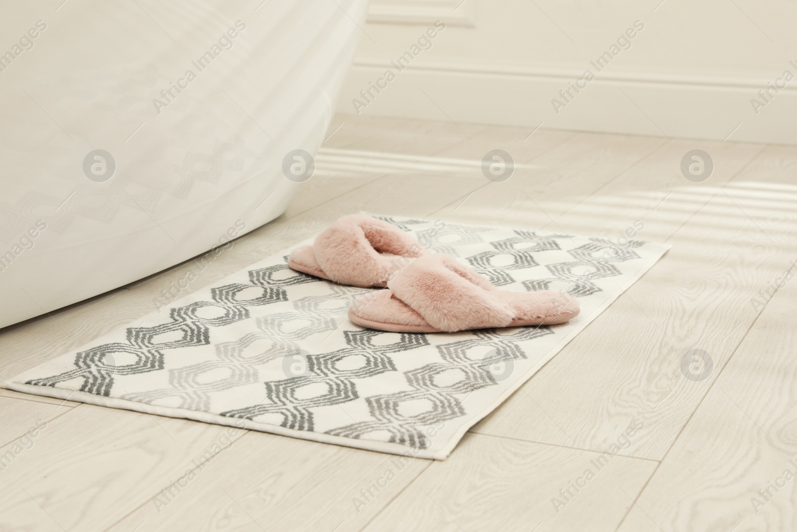 Photo of New bath mat with fluffy slippers near tub indoors