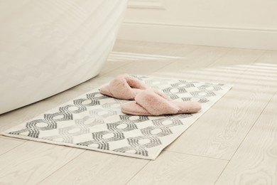 Photo of New bath mat with fluffy slippers near tub indoors