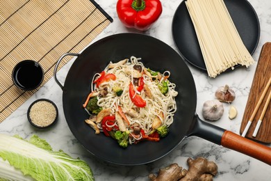 Photo of Stir fried noodles with chicken and vegetables in wok on white marble table, flat lay