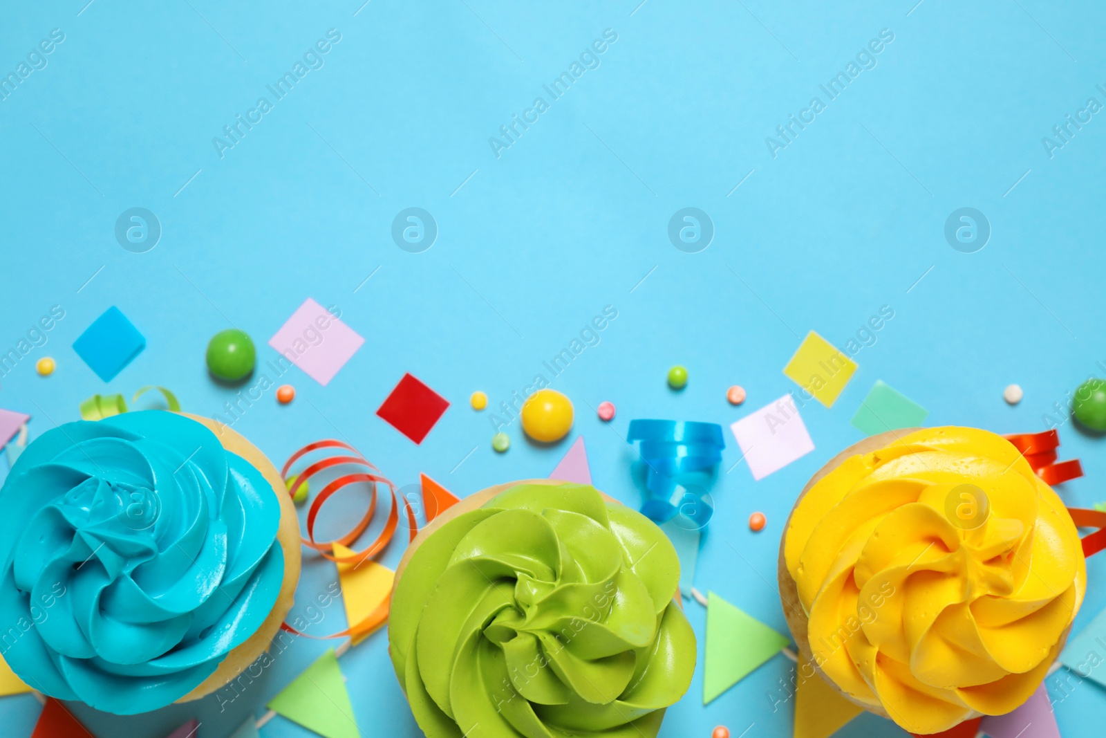 Photo of Colorful birthday cupcakes on light blue background, flat lay. Space for text