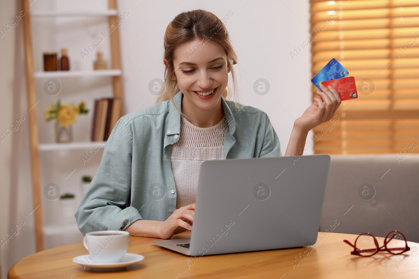 Photo of Woman with credit cards using laptop for online shopping at wooden table indoors