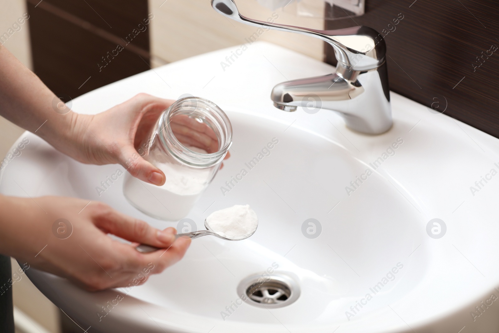 Photo of Woman using baking soda to unclog sink drain in bathroom, closeup