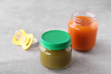 Photo of Jars with healthy baby food and pacifier on light grey table