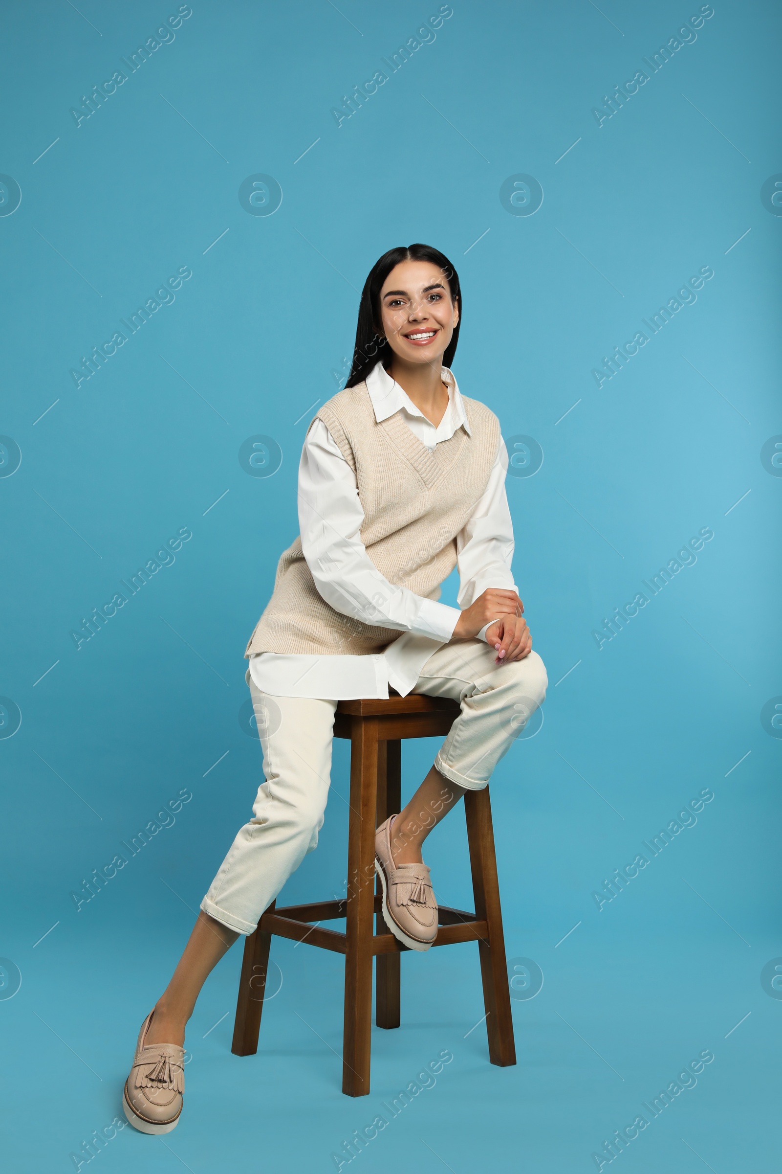 Photo of Beautiful young woman sitting on stool against turquoise background