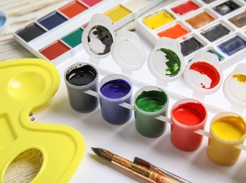 Photo of Different paints, brushes and palette on wooden table, closeup