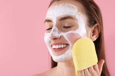 Photo of Happy young woman washing off face mask with sponge on pink background. Space for text