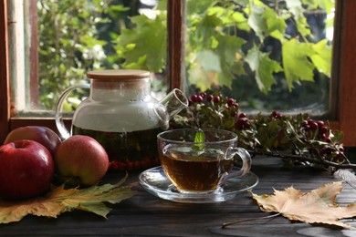 Photo of Hot tea, apples and dry leaves on wooden windowsill. Autumn atmosphere