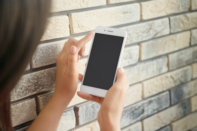 Photo of Young woman holding mobile phone with blank screen in hand near brick wall